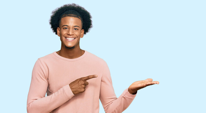 African american man with afro hair wearing casual clothes amazed and smiling to the camera while presenting with hand and pointing with finger.
