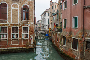 Fototapeta na wymiar View of a small canal in Venice with old houses with Venetian flags. Gloomy winter day.