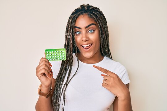 Young african american woman with braids holding birth control pills smiling happy pointing with hand and finger