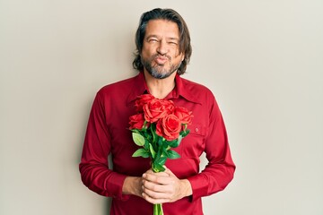 Middle age handsome man holding bouquet of red roses looking at the camera blowing a kiss being lovely and sexy. love expression.