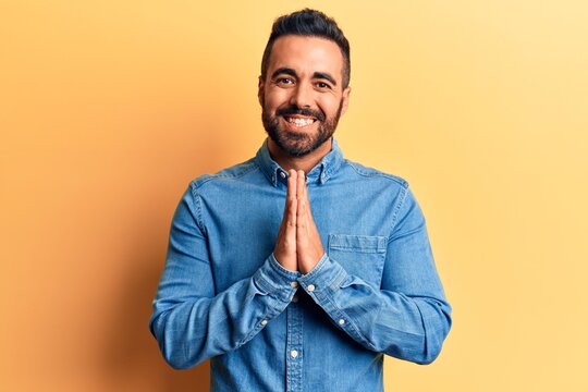 Young hispanic man wearing casual clothes praying with hands together asking for forgiveness smiling confident.