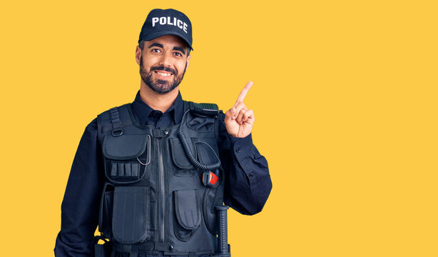 Young hispanic man wearing police uniform with a big smile on face, pointing with hand finger to the side looking at the camera.
