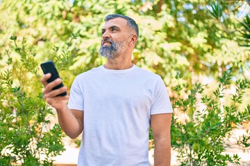 Middle age grey-haired man smiling happy using smartphone at the park