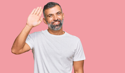 Fototapeta premium Middle age handsome man wearing casual white tshirt waiving saying hello happy and smiling, friendly welcome gesture
