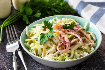 Salad with fresh cabbage, cucumber, green peas and octopus in a bowl on a dark countertop.