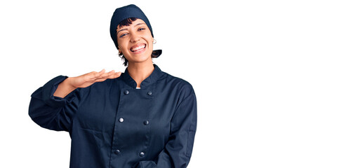Young brunette woman with short hair wearing professional cook uniform gesturing with hands showing big and large size sign, measure symbol. smiling looking at the camera. measuring concept.