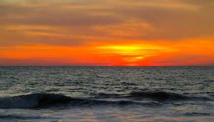 A beautiful red and orange sunset over the Pacific Ocean the silhouettes of beachgoers outlined against the water of Puerto Escondito, Mexico.  Image has copy space.