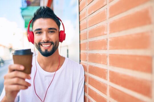 Young arab man drinking take away coffee and using headphones at the city.