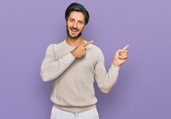 Young hispanic man wearing casual clothes smiling and looking at the camera pointing with two hands and fingers to the side.