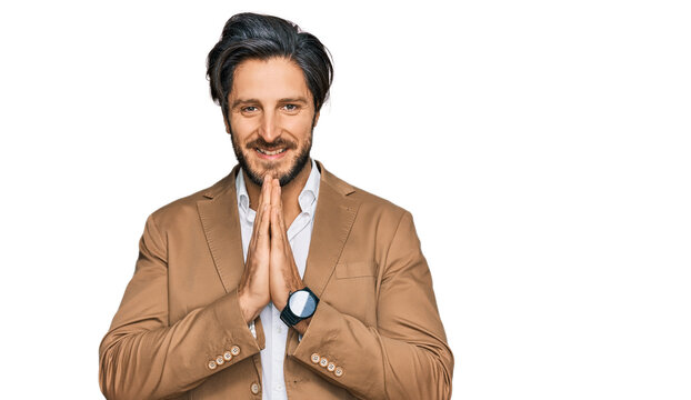 Young hispanic man wearing business clothes praying with hands together asking for forgiveness smiling confident.
