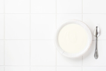 Greek yogurt in white bowl, linen napkin and wooden spoon on white table. Top view.