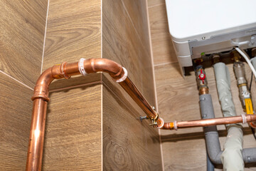 Copper pipes for natural gas installations, attached to a wall in a boiler room lined with ceramic...