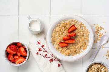Simple oatmeal porridge with strawberries in a white plate on a linen napkin. Breakfast health food concept. Top view.