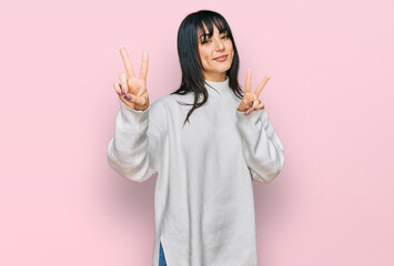 Young brunette woman with bangs wearing casual turtleneck sweater smiling looking to the camera showing fingers doing victory sign. number two.