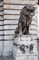 A sculpture of a lion made of stone on a white pedestal against the background of a building wall.