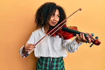 Beautiful african american woman with afro hair playing classical violin smiling looking to the...