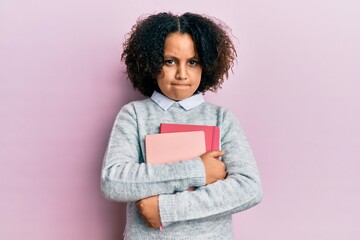 Young little girl with afro hair holding books skeptic and nervous, frowning upset because of...