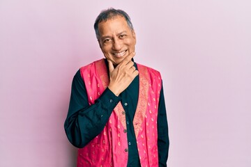 Middle age indian man wearing traditional indian clothes looking confident at the camera smiling with crossed arms and hand raised on chin. thinking positive.