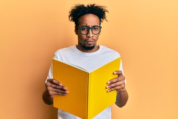 Young african american man with beard reading a book wearing glasses skeptic and nervous, frowning...