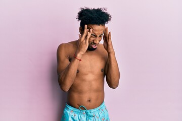 Fototapeta premium Young african american man with beard wearing swimsuit with hand on head for pain in head because stress. suffering migraine.