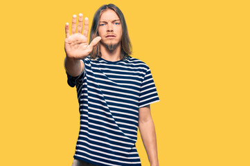 Handsome caucasian man with long hair wearing casual striped t-shirt doing stop sing with palm of...