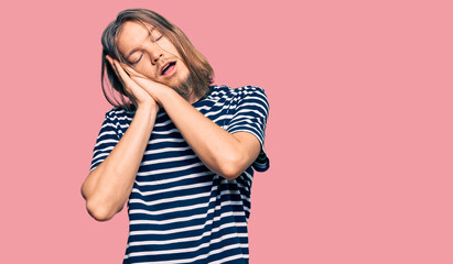 Handsome caucasian man with long hair wearing casual striped t-shirt sleeping tired dreaming and posing with hands together while smiling with closed eyes.