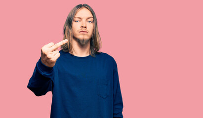 Handsome caucasian man with long hair wearing casual winter sweater showing middle finger, impolite...