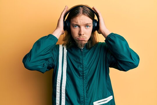 Handsome caucasian man with long hair wearing gym clothes and using headphones depressed and worry for distress, crying angry and afraid. sad expression.
