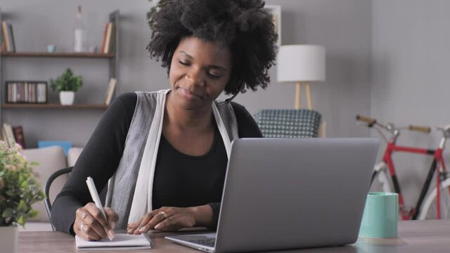 Smiling black woman student at the computer e-learning study with online teacher,young african american female talking in video call conference chat,virtual tutor using laptop at her desk from home
