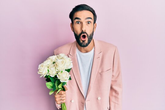 Young hispanic man holding flowers scared and amazed with open mouth for surprise, disbelief face