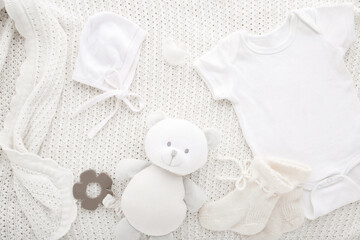 Newborn bodysuit, hat, socks, soother and teddy bear on light white blanket background. Closeup. Preparing baby clothes. Top down view.