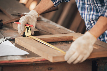 closeup man carpenter measuring wood with tape measure in workshop