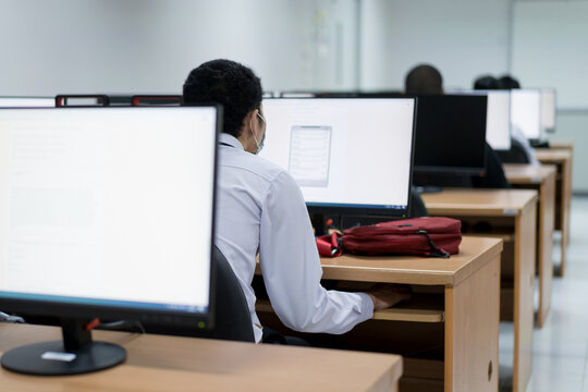Blur and selective focus of the adult university learners wearing a face mask while concentrating on doing online examination in the computer room. Serious students working on computer at university