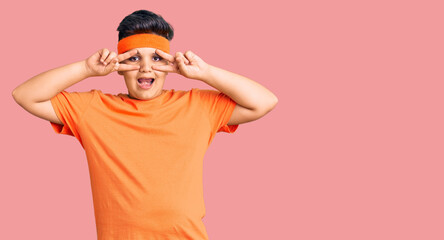 Little boy kid wearing sportswear doing peace symbol with fingers over face, smiling cheerful showing victory