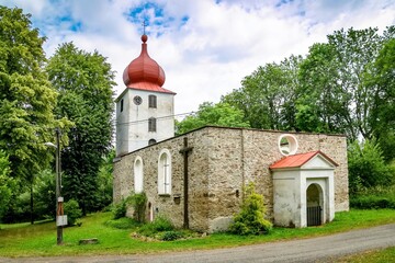 Vysoka, Czech Republic - July 6 2018: View of the preserved ruin of church of John the Baptist built in 13th century, white tower with clock, red roof and perimeter stone walls with windows.
