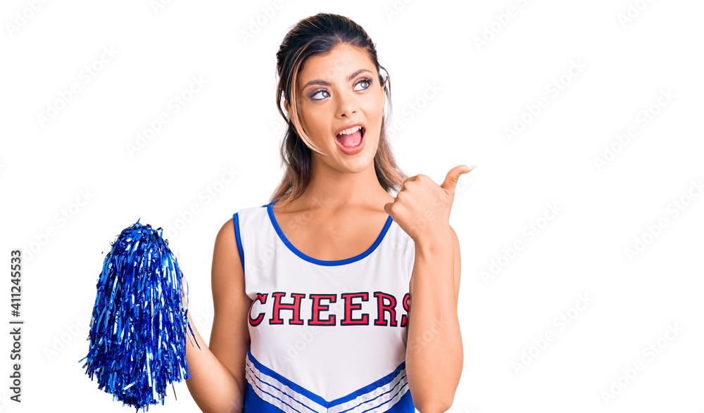 Canvas Prints Young beautiful woman wearing cheerleader uniform smiling with happy face looking and pointing to the side with thumb up.