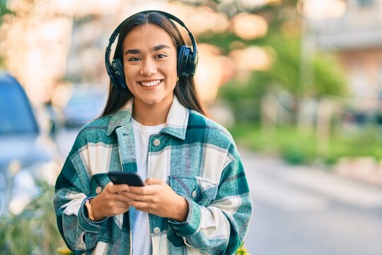 Young latin girl smiling happy using smartphone and headphones at the city.