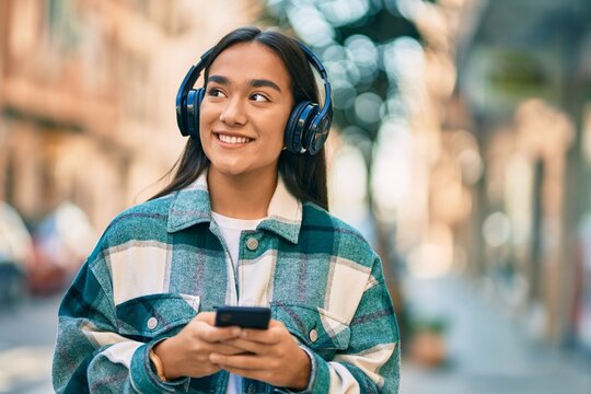 Young latin girl smiling happy using smartphone and headphones at the city.