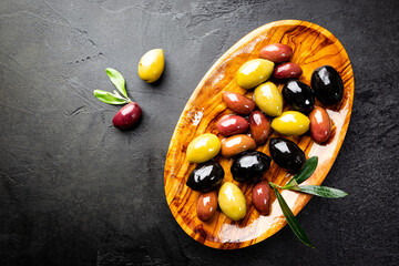Black and green olives and olive oil in wooden bowls on black background. Top view with copy space for text.