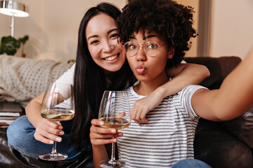 Dark-skinned woman in stylish clothes and with beautiful curly hair makes cool selfie with her friend