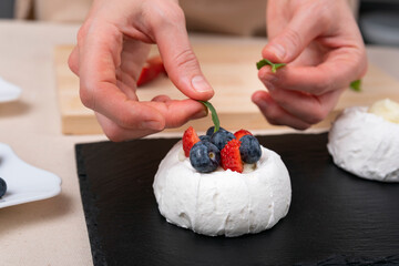 Obraz na płótnie Canvas Womens hands decorate cake. Fresh berries and white meringue.