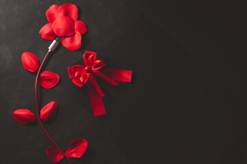 Concept shape, love, technology Red smartphone charging cable and rose petals on black background