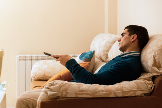 
bored young man watching tv while sitting on the sofa in his apartment