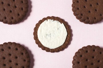 On a pastel pink background in the center lay a chocolate-cream cookie broken in half. Next to it in the corners are four whole cookies.