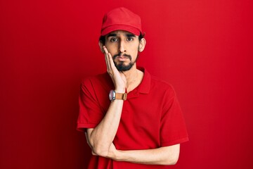 Young hispanic man wearing delivery uniform and cap thinking looking tired and bored with depression problems with crossed arms.