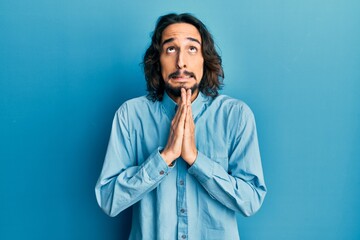 Young hispanic man wearing casual clothes begging and praying with hands together with hope...
