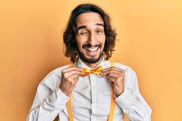 Young hispanic man wearing hipster elegant look holding bowtie winking looking at the camera with...