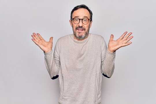 Middle age handsome man wearing casual sweater and glasses over isolated white background clueless and confused with open arms, no idea and doubtful face.