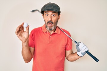 Middle age hispanic man holding golf club and ball clueless and confused expression. doubt concept.
