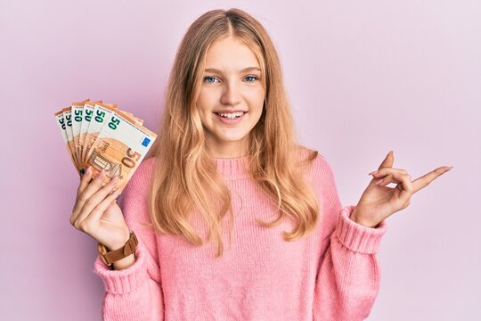 Beautiful young caucasian girl holding bunch of 50 euro banknotes smiling happy pointing with hand and finger to the side